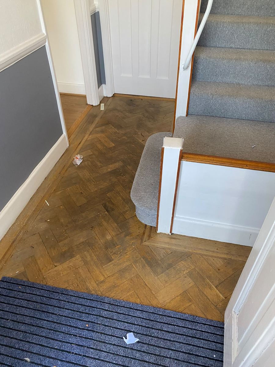 Hallway parquet before cleaning, with litter and dust across the floor